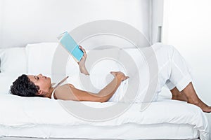 Pregnant woman reading a book while lying on a bed