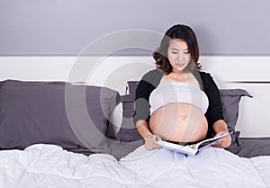 Pregnant woman reading a book while lying on a bed in the bedroo