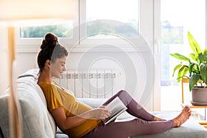 Pregnant woman reading book on sofa at home