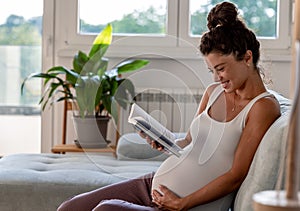 Pregnant woman reading book on sofa at home
