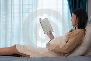 Pregnant woman reading a stories to her unborn child in the living room