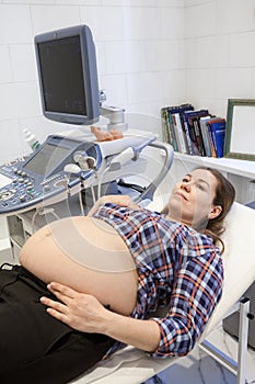 Pregnant woman ready for ultrasound and screening procedures. Medical equipment, scanner and monitor are in inspection room