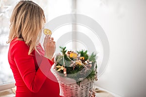 A pregnant woman in a red dress decorates for the New Year. A woman waiting for a baby in a red dress in a bright room by the Chri