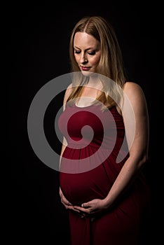 Pregnant woman in red dress holding belly on black background