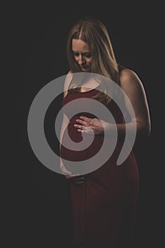 Pregnant woman in red dress holding belly on black background