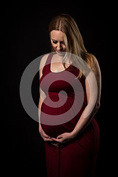 Pregnant woman in red dress holding belly on black background