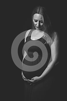 Pregnant woman in red dress holding belly on black background