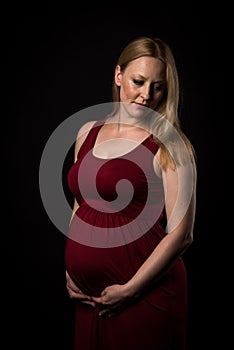 Pregnant woman in red dress holding belly on black background