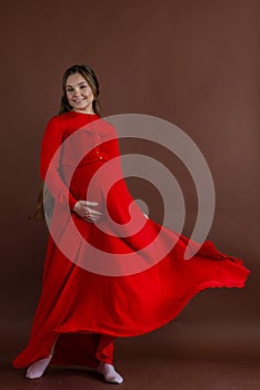 Pregnant woman in red flying dress holding her belly