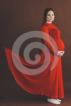 Pregnant woman in red flying dress holding her belly