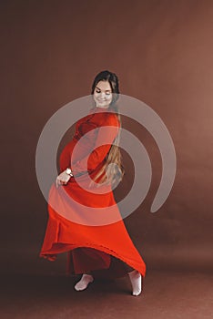 Pregnant woman in red flying dress holding her belly