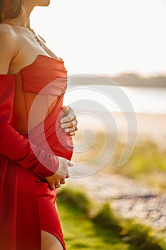 a pregnant woman in a red tight dress stroking her tummy with her hands.