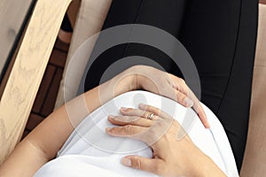pregnant woman relaxed and enjoys pregnancy, young happy pregnant woman hugging her belly with her hands, top view