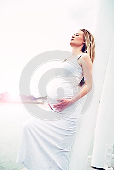 Pregnant woman relaxing against a white pillar