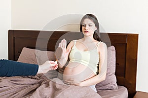 Pregnant woman relaxing in bed rejects to eat an ice cream. No sweet during pregnancy. Healthy diet of expecting mother concept