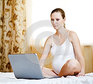 Pregnant woman relaxing with her laptop on a bed