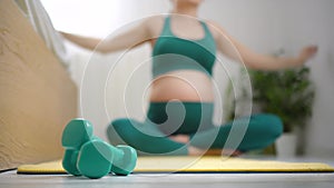 Pregnant woman relaxing after sport. Girl on background stretching, focus on foreground at dumbbells