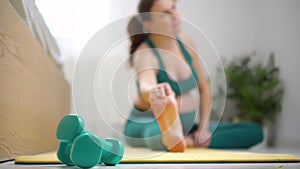 Pregnant woman relaxing after sport. Girl on background stretching, focus on foreground at dumbbells