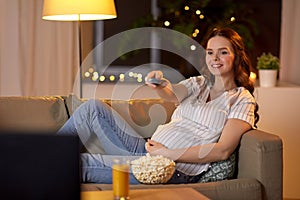 Pregnant woman with remote control watching tv