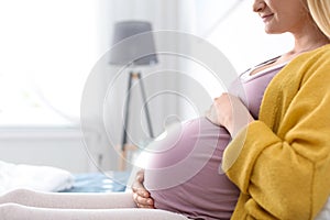 Pregnant woman resting on bed in light room, closeup