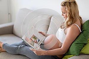 Pregnant woman resting and reading book on sofa