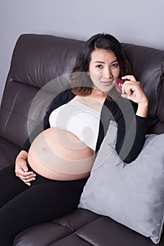 Pregnant woman resting with red apple at home on sofa