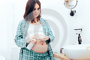 Pregnant Woman Rubbing Cream Anti-Stretchmarks on her Stomach photo