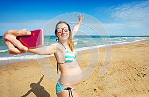Pregnant woman on sea beach do selfie with phone