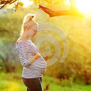Pregnant woman on second trimester posing in sunny garden in the backlit photo