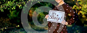 Pregnant woman on second trimester posing in sunny garden, shows a slogan its a boy