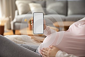 Pregnant woman showing blank smartphone screen while resting on couch