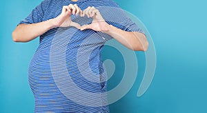 Pregnant woman showing heart shape gesture with fingers on blue isolated background