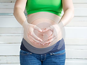 Pregnant woman showing heart shape with hands in front of stomach