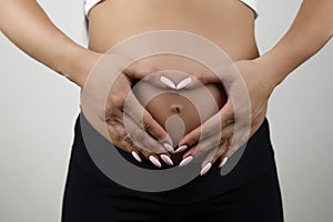 Pregnant woman showing heart sign with her hands on her pregnant belly isolated white background