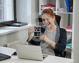 A pregnant woman shows a photo from an ultrasound scan of the fetus via video link in the office.