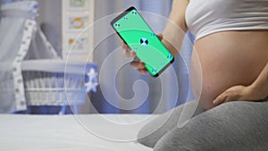 Pregnant woman shows a smartphone with a green screen.