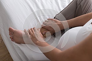 Pregnant woman sit on bed touch, massages her swollen foot