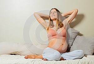 Pregnant woman sit smiling with hands behind head