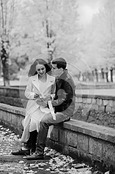 A pregnant woman sits on her husband's lap and holds small baby socks in her hands.