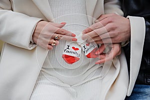 A pregnant woman sits on her husband's lap and holds small baby socks in her hands.