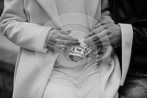 A pregnant woman sits on her husband's lap and holds small baby socks in her hands.