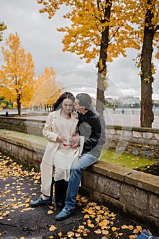 A pregnant woman sits on her husband& x27;s lap and holds small baby socks in her hands.