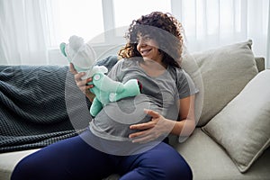 A pregnant woman sits on a sofa with a child& x27;s toy rabbit for Easter in her hands smile. Lifestyle of a pregnant