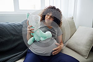 A pregnant woman sits on a sofa with a child& x27;s toy rabbit for Easter in her hands smile. Lifestyle of a pregnant