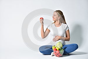 A pregnant woman sits on a white background and wants to eat a tomato