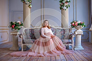 A pregnant woman sitting in a beautiful dress on the couch. the concept of motherhood