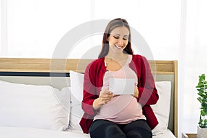 Pregnant woman sitting on bed and looking at her ultrasound image of her child in her belly