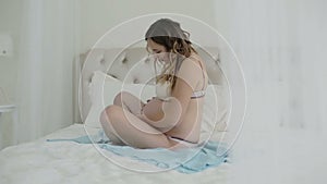 Pregnant woman sitting on a bed and stroking her belly.