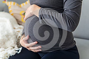 Pregnant woman sitting comfortably on the sofa and resting while putting her hands on her belly.