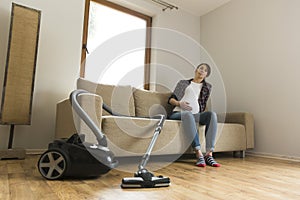 Pregnant woman sitting on couch tired of vacuuming. Household and spring cleaning concept